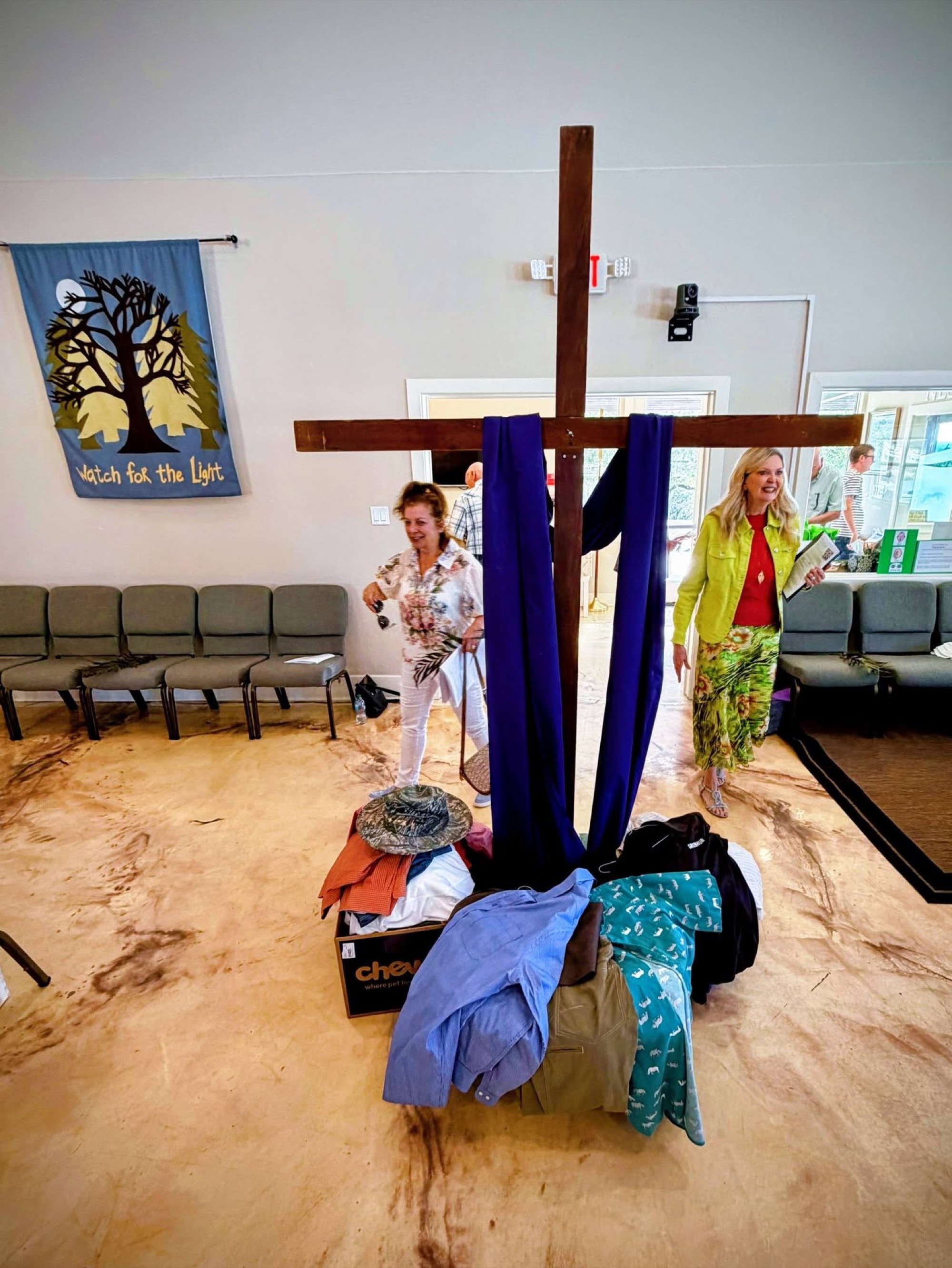 A wooden cross draped in purple surrounded by donated clothing collected in the sanctuary.